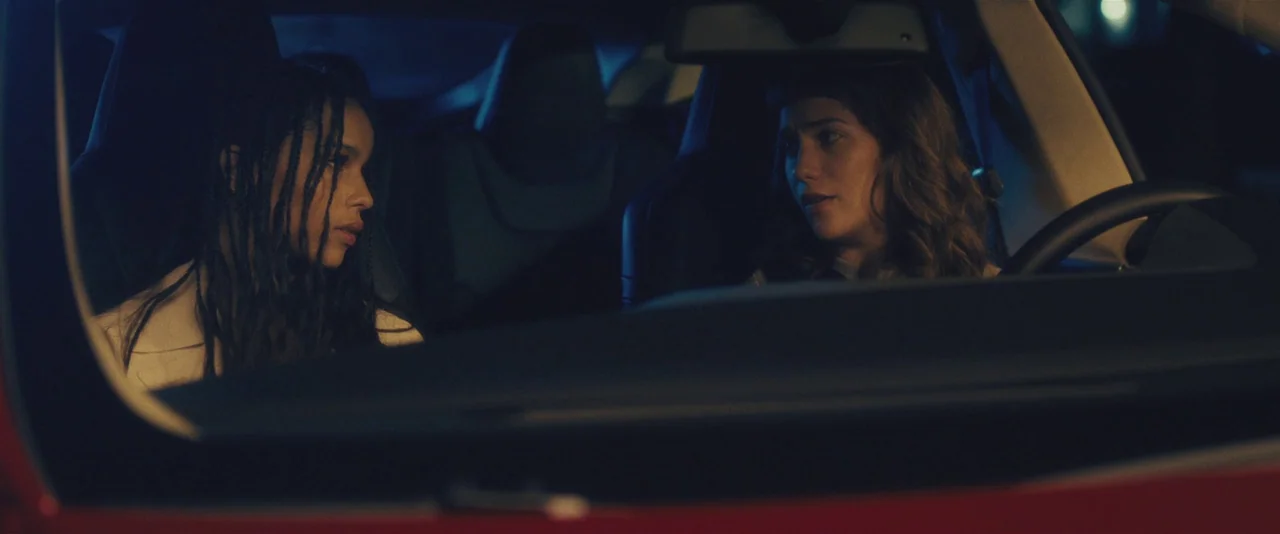 Gemini (2017) movie still: medium — Two women sit in the front seats of a modern vehicle at night. They face each other while engaged in a…