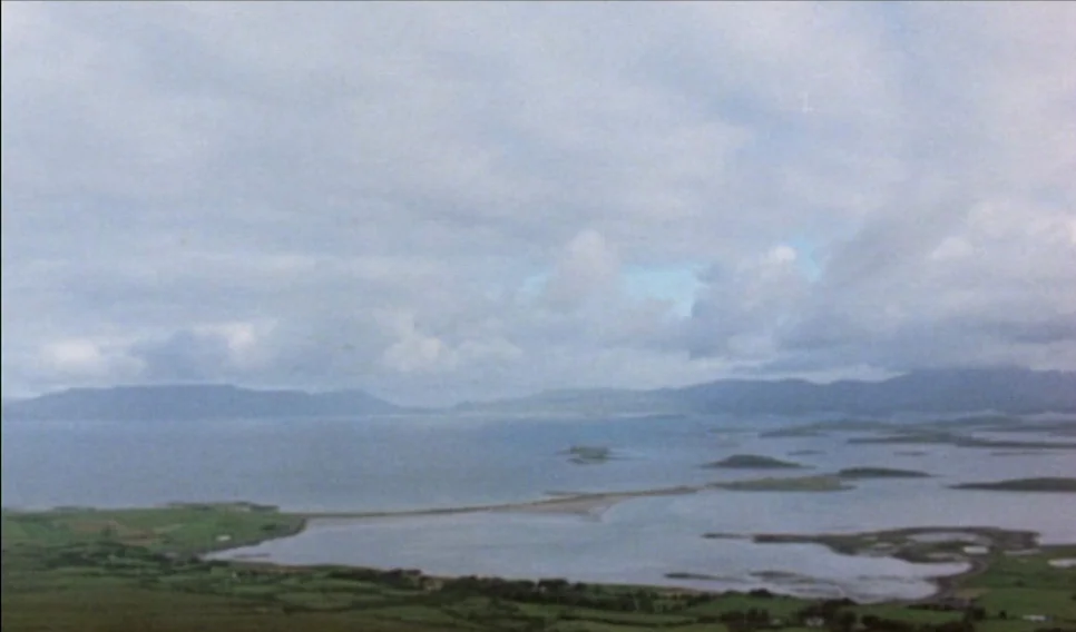Heart of Glass (1976) movie still: establishing — A wide coastal landscape shows a large bay with small islands and grassy peninsulas. An overcast…