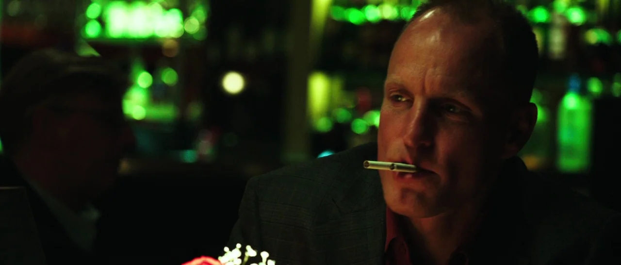 Rampart (2011) movie still: medium — A dimly lit drinking establishment features out-of-focus bottles glowing with bright green neon light. A man in…