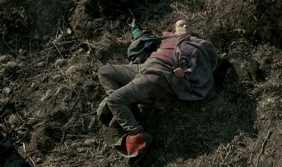 Vagabond (1985) movie still: fullbody — A person lies on a barren, uneven patch of earth covered in dry debris. The individual rests on the ground…