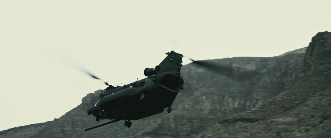12 Strong (2018) movie still: wide — A military transport helicopter maneuvers through a rugged and rocky mountain canyon. The large aircraft…