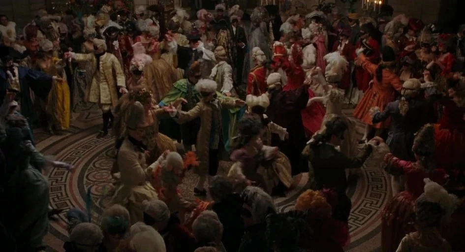 Marie Antoinette (2006) movie still: wide — A large indoor ballroom with a decorative circular floor pattern hosts a masquerade dance. A crowd of…
