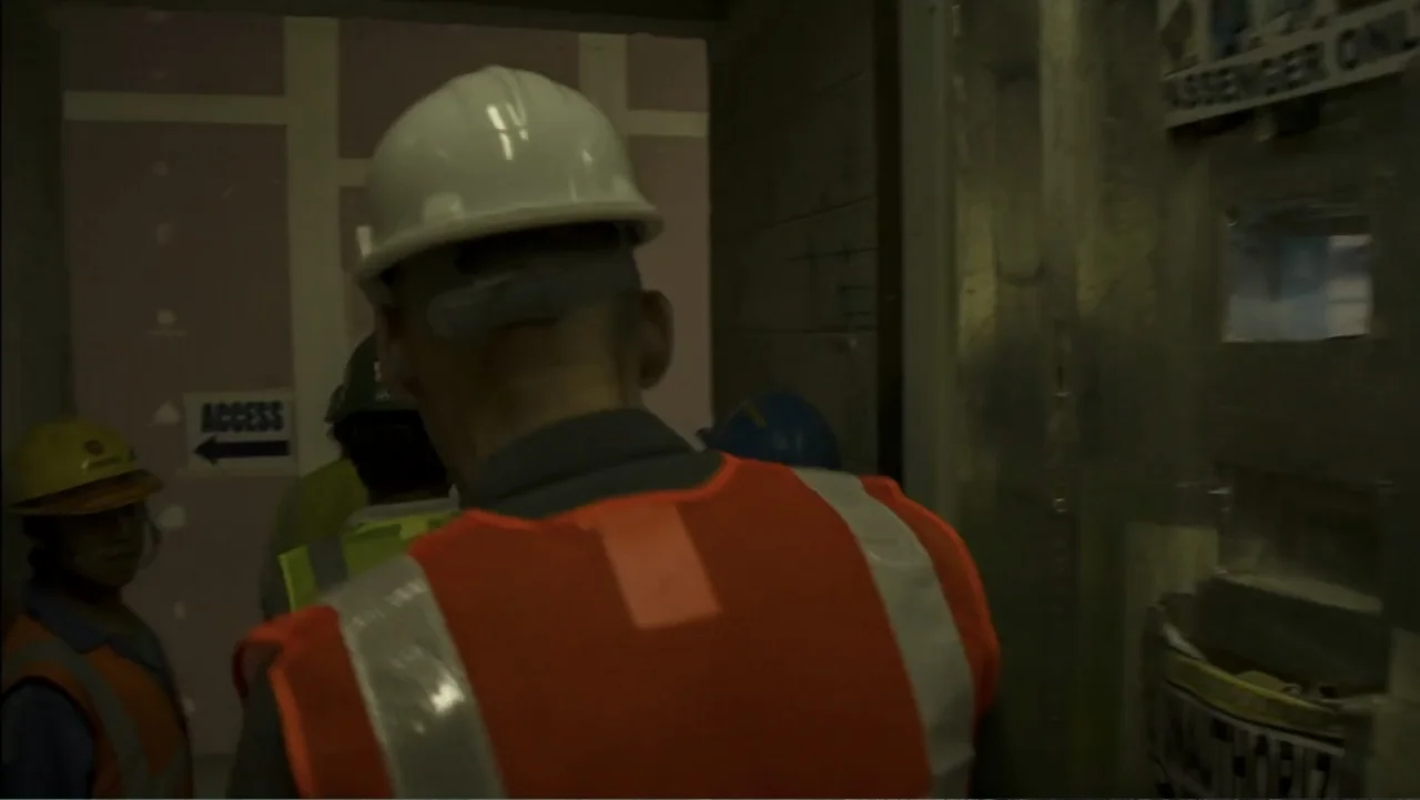 REM (2019) movie still: medium — A dimly lit construction area features unfinished walls and industrial signage. Several individuals wearing…