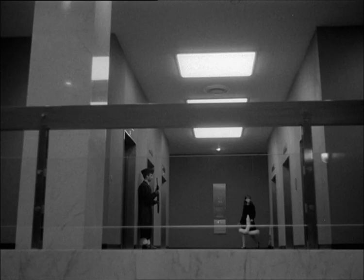 Alphaville (1965) movie still: wide — An office lobby features minimalist walls, clean lines, and multiple stainless steel elevator doors. A…