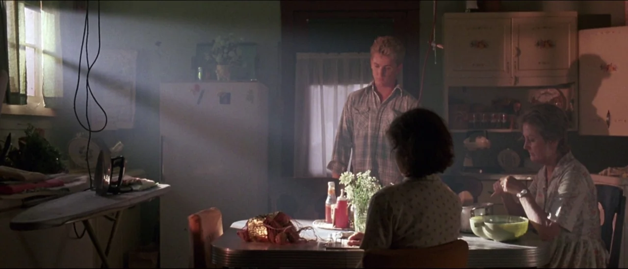 At Close Range (1986) movie still: wide — A modest home kitchen with vintage appliances, wooden cabinets, and an ironing board setup. A group of…