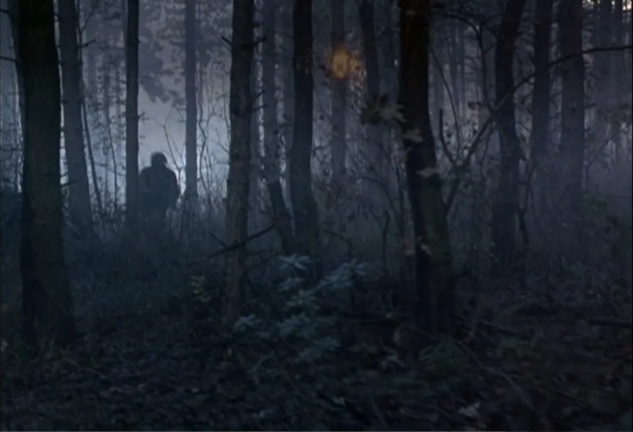 When Trumpets Fade (1998) movie still: wide — A dark dense wood at night is filled with thick fog and tall trees. A single silhouetted figure walks…