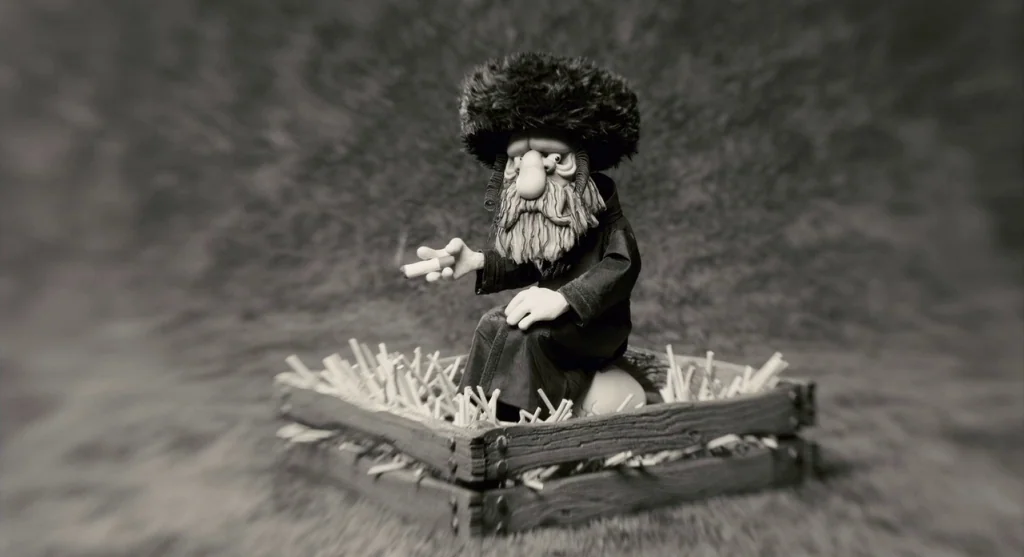 Mary & Max (2009) movie still: fullbody — A stop-motion figure sits in a wooden crate filled with small white sticks. The surrounding background is…