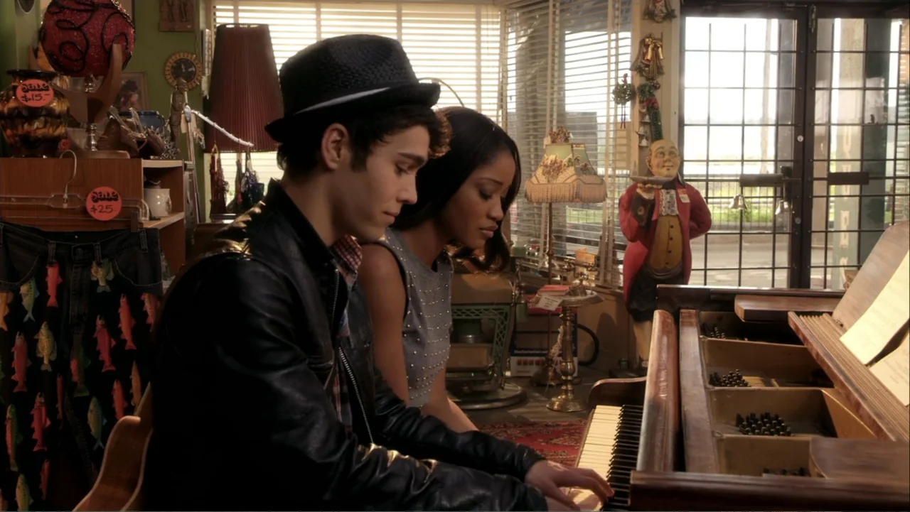 Rags (2012) movie still: medium — A cluttered shop interior filled with second-hand merchandise and a vintage piano. A teenage couple sits at the…