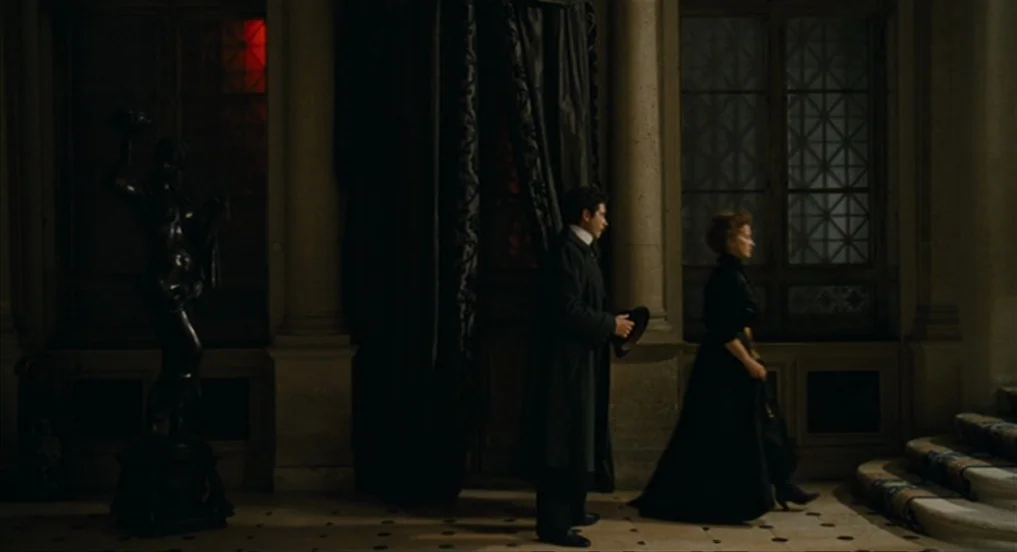 House of Tolerance (2011) movie still: wide — A spacious, dimly lit interior hall features stone floors and ornate classical windows. A man in a…