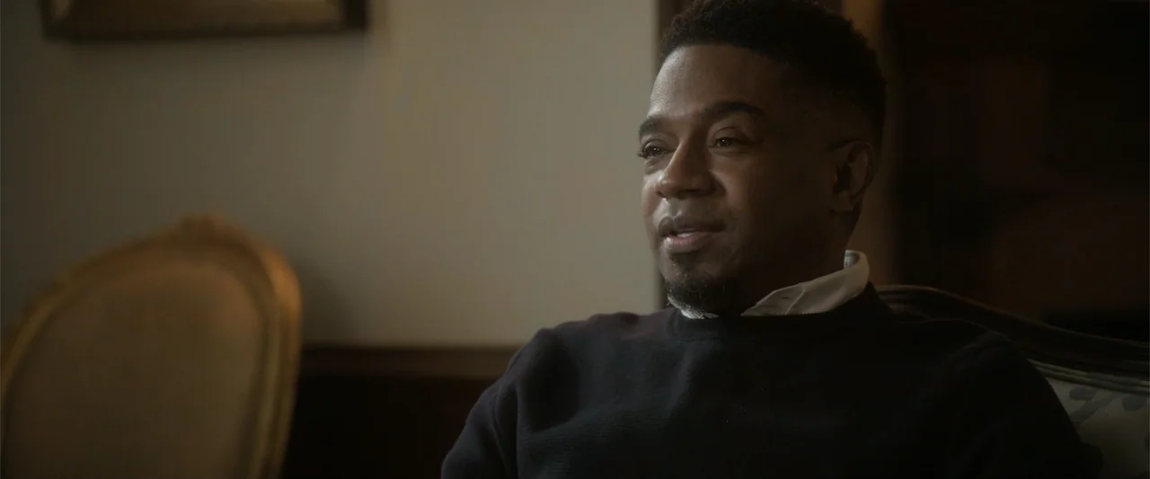 Maxine's Baby: The Tyler Perry Story (2023) movie still: medium — A dimly lit indoor room features a single upholstered wooden chair. A man wearing…
