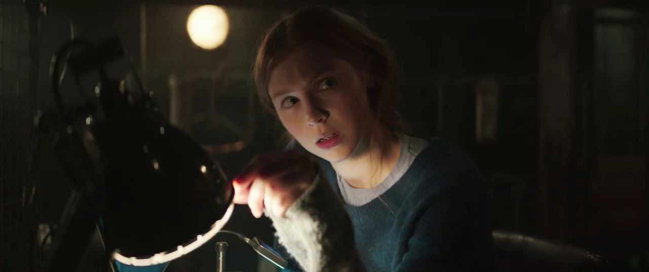 Sea Fever (2019) movie still: medium — A dark, dimly lit workspace with a single focus light illuminating a person. The subject adjusts the angle of…