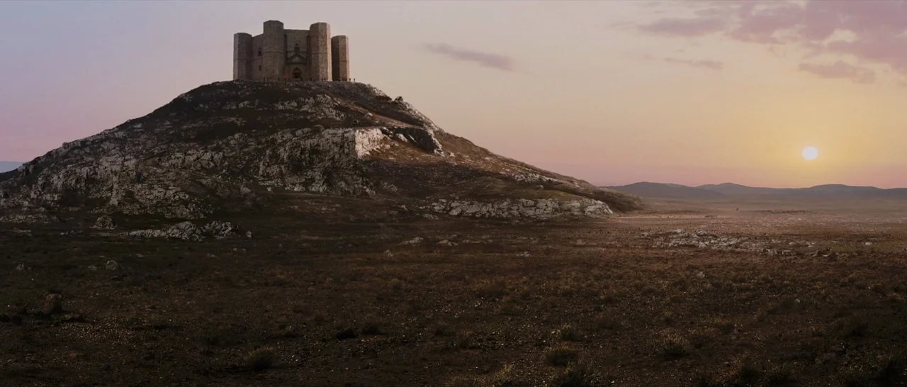 Tale of Tales (2015) movie still: establishing — A stone medieval fortress rests on the peak of a rocky, sparse hill. The surrounding flat terrain…
