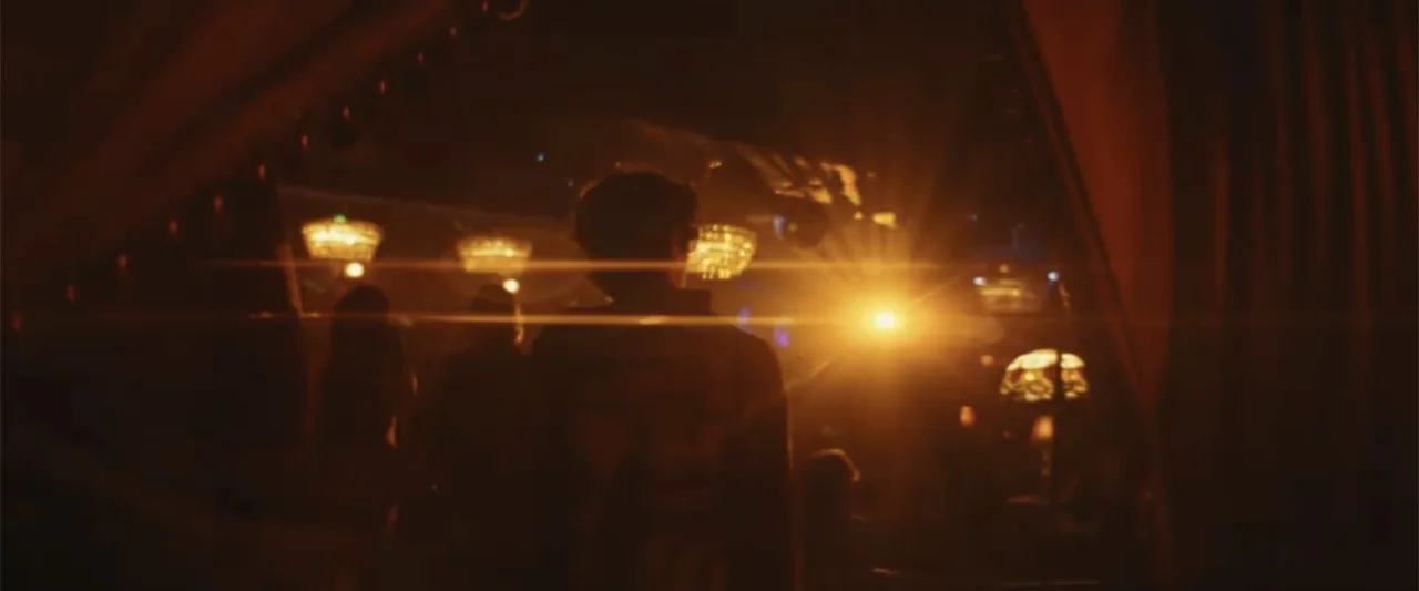Anora (2024) movie still: medium — A dimly lit interior space features numerous hanging lamps and heavy fabric curtains. A person stands facing away…