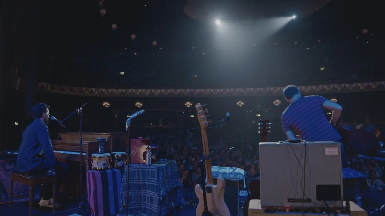 Flight of the Conchords: Live in London (2018) movie still: wide — A large concert stage holds a wooden piano and various musical equipment in dim…