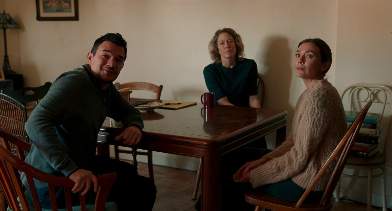 His Three Daughters (2023) movie still: medium — Three people sit around a polished wooden table in a brightly lit room. They appear to be engaged…