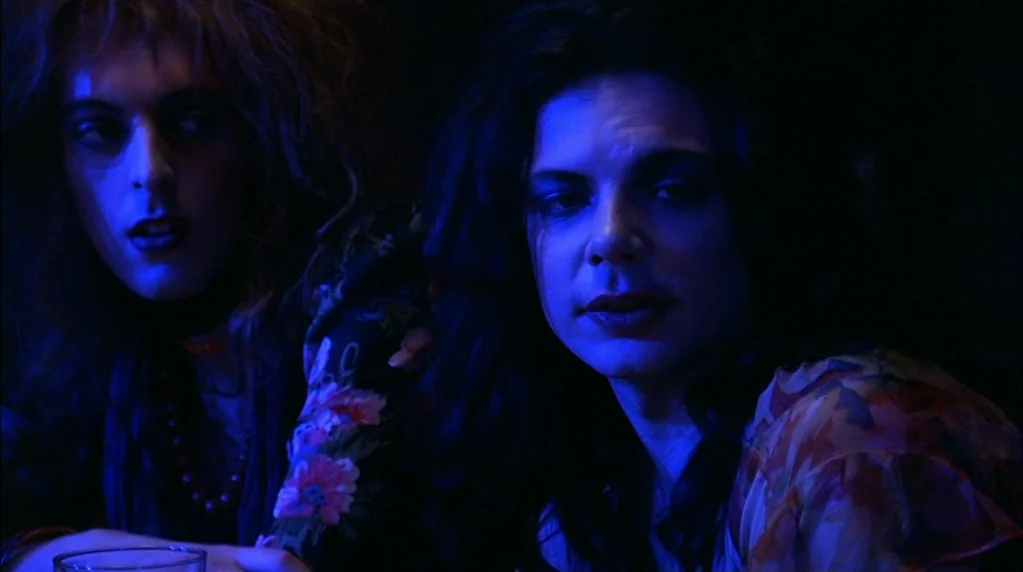 Velvet Goldmine (1998) movie still: medium — A dark, dimly lit environment features two people with theatrical hair and makeup. The subjects sit…
