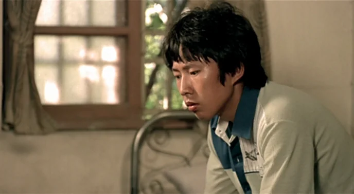 The Boys From Fengkuei (1983) movie still: medium — An indoor room features a metal bed frame against a window with curtains. A young man sits in…