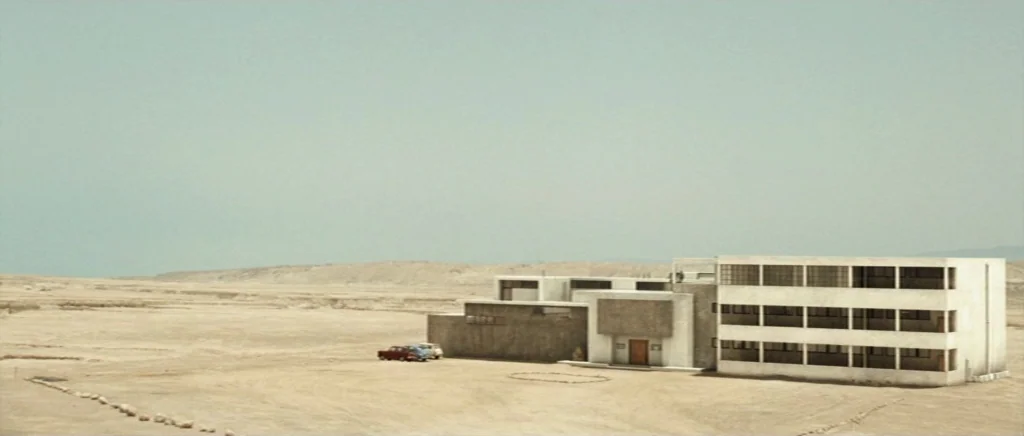 Adam Resurrected (2008) movie still: establishing — A low-rise modernist concrete structure stands isolated within a vast, featureless arid desert…