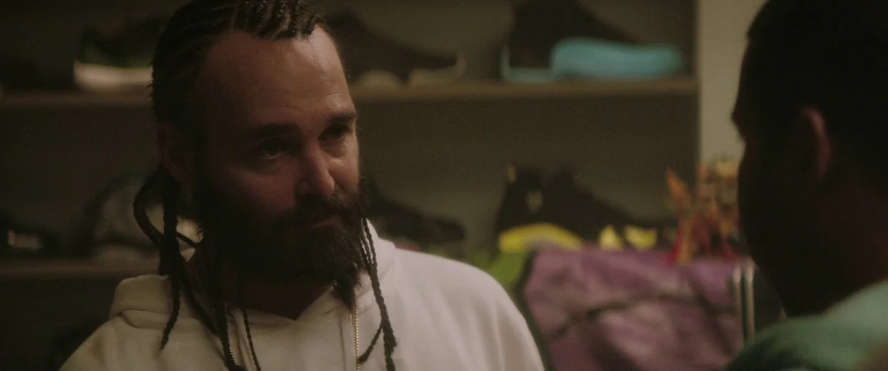 Keanu (2016) movie still: medium — Shelves filled with various sneakers line the wall behind the main subject. A bearded man in a white hoodie…