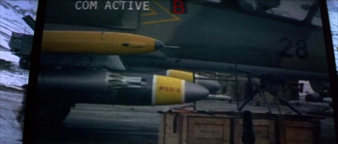 Tomorrow Never Dies (1997) movie still: wide — A military jet with yellow-banded missiles is parked on an icy, gray concrete tarmac. A digital…