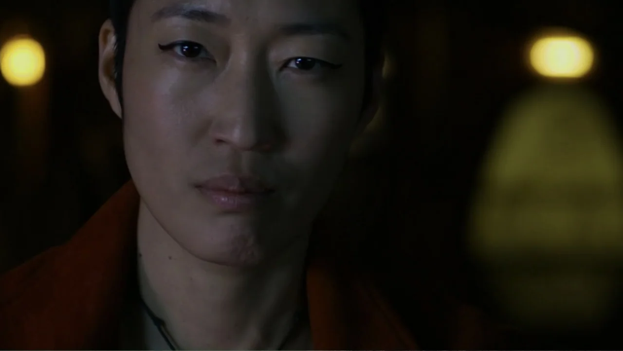 Mortal Engines (2018) movie still: closeup — A dimly lit interior space features a dark background with blurred yellow bokeh lights. A woman with…