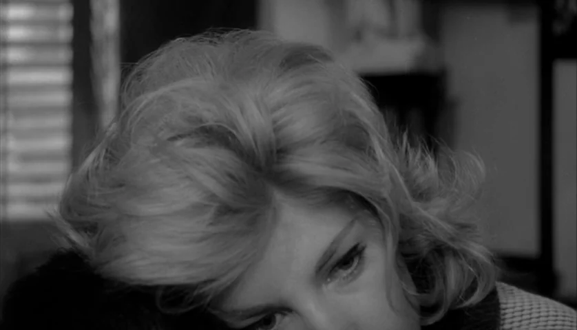 L’Avventura (1960) movie still: closeup — A close view of a blonde woman inside a dimly lit room. She rests her head downward while looking toward…