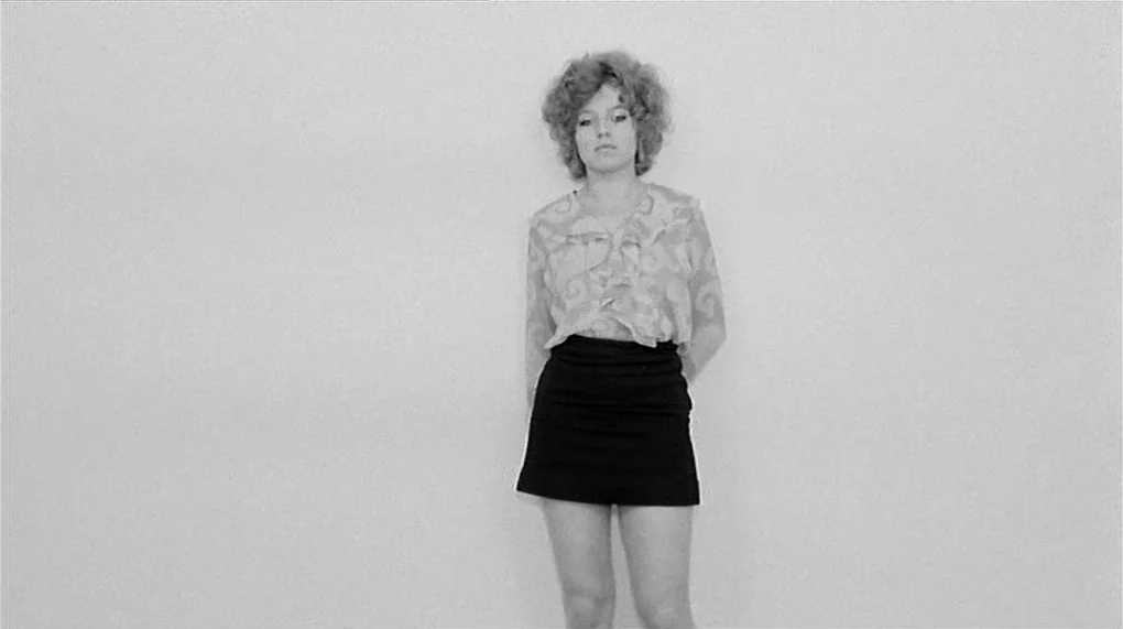 Love Is Colder Than Death (1969) movie still: fullbody — A woman stands against a stark, featureless white wall in a minimalist space. She stands…