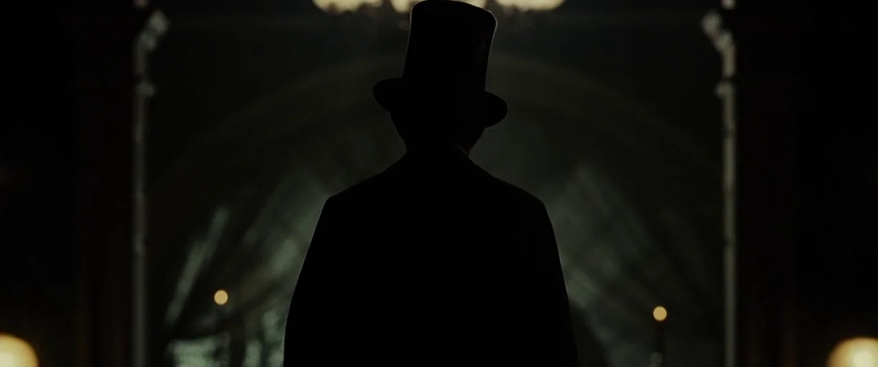 Lincoln (2012) movie still: medium — A dark foyer with shadowy architectural arches and flickering candles in the distant background. A man wearing…