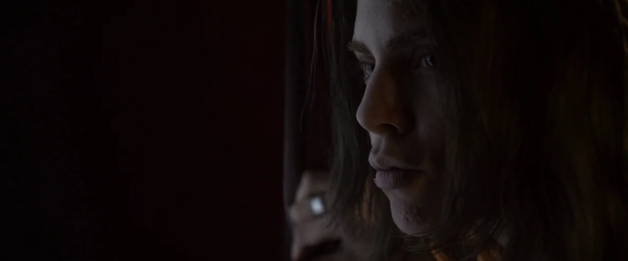 Excision (2012) movie still: closeup — A dark, dimly lit interior space with heavy curtains blocking most incoming light. A young man with long hair…