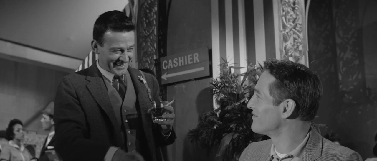 The Hustler (1961) movie still: medium — Two men converse in a dimly lit restaurant with a cashier sign visible. One man holds a drink and cigarette…