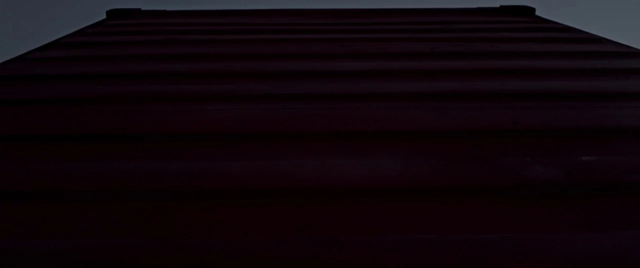 All Is Lost (2013) movie still: establishing — A close-up of the corrugated steel surface of a dark red shipping container. The ribbed metal panels…