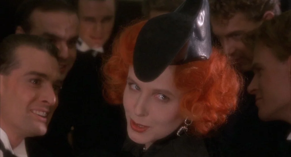Brazil (1985) movie still: closeup — A dimly lit room filled with several men in formal evening wear and black suits. A woman with bright red hair…