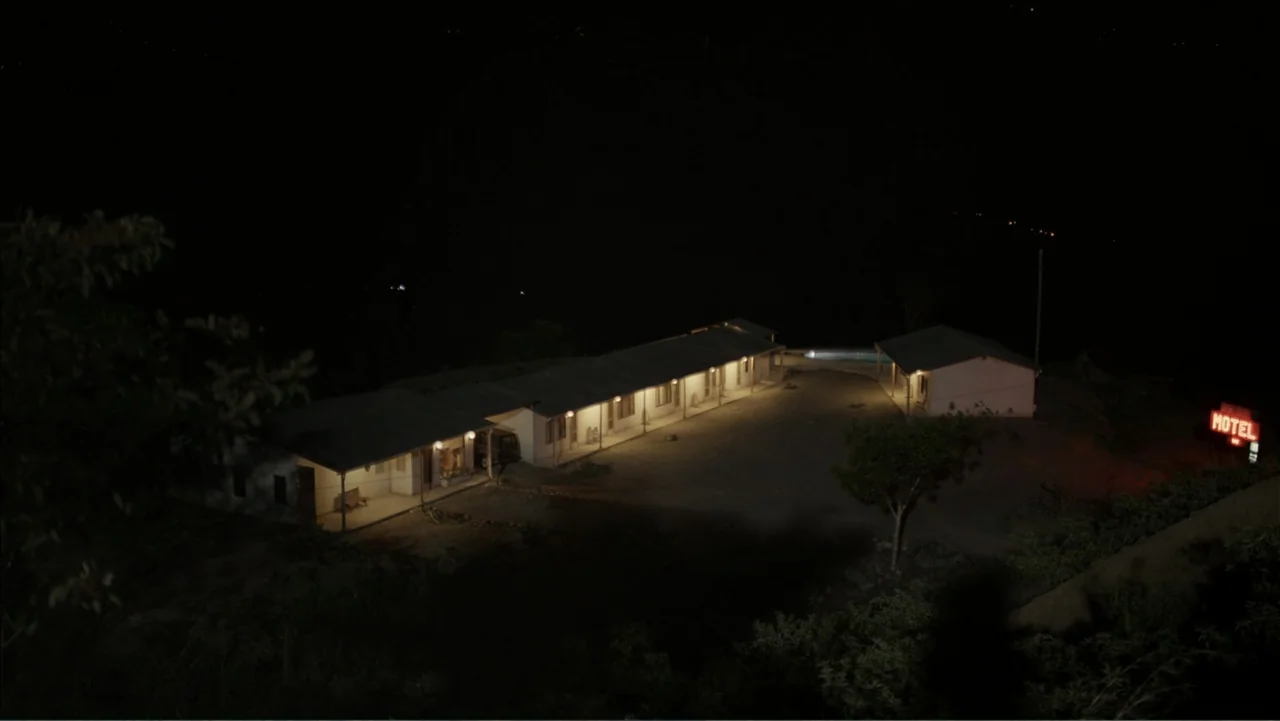 Boy (2010) movie still: establishing — A single-story motel complex sits in a dark, isolated landscape at night. The motel exterior is lit by small…