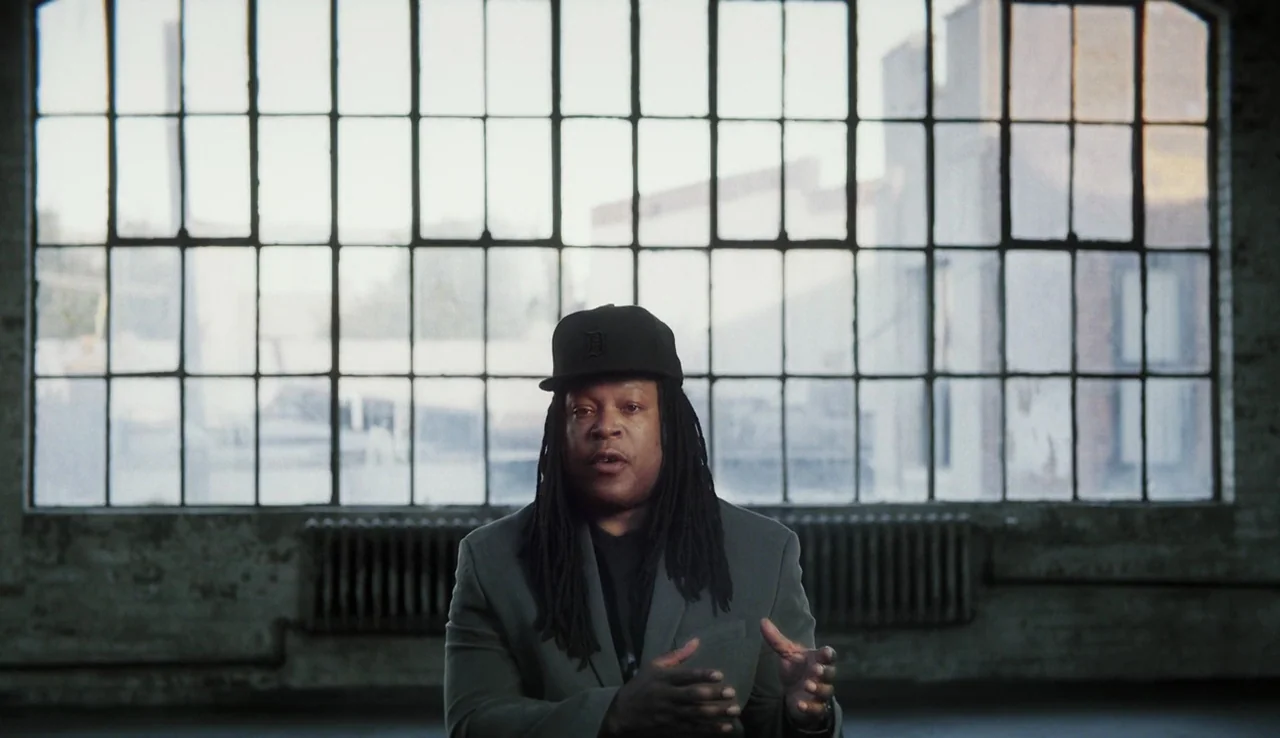 13th (2016) movie still: medium — A spacious room features a large window divided by metal frames overlooking a city. A man stands in the foreground…