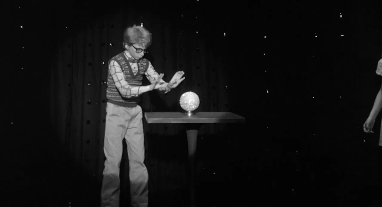 Stardust Memories (1980) movie still: fullbody — A dark stage features a black backdrop decorated with subtle light pinpoints. A young boy in a…