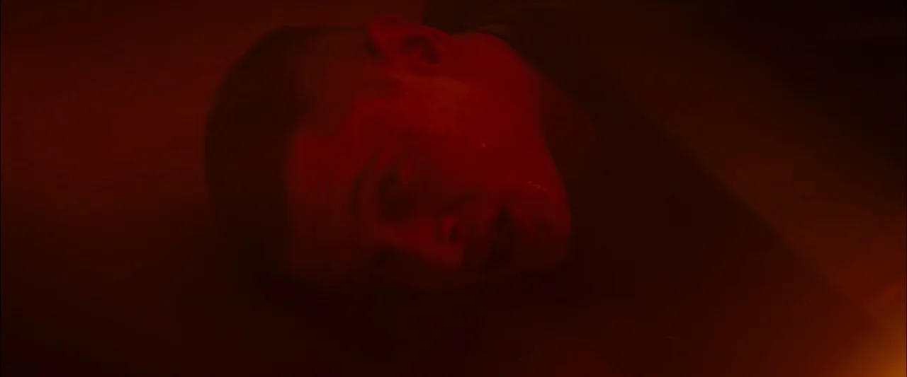 Starred Up (2013) movie still: closeup — A dark environment is filled with an intense red ambient glow. A man lies horizontally on a flat surface…