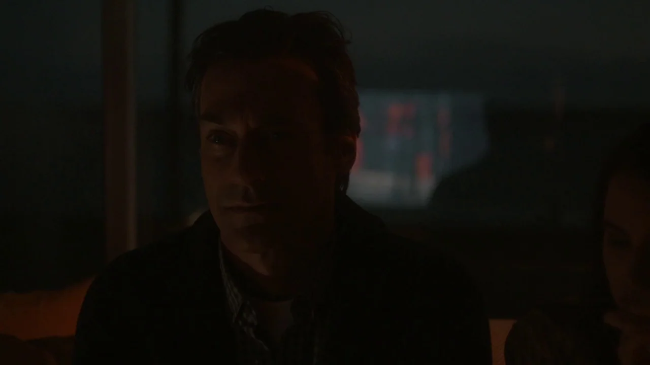 Marjorie Prime (2017) movie still: medium — A dark, sparsely lit living room at night with minimal interior features visible. A man looks toward an…