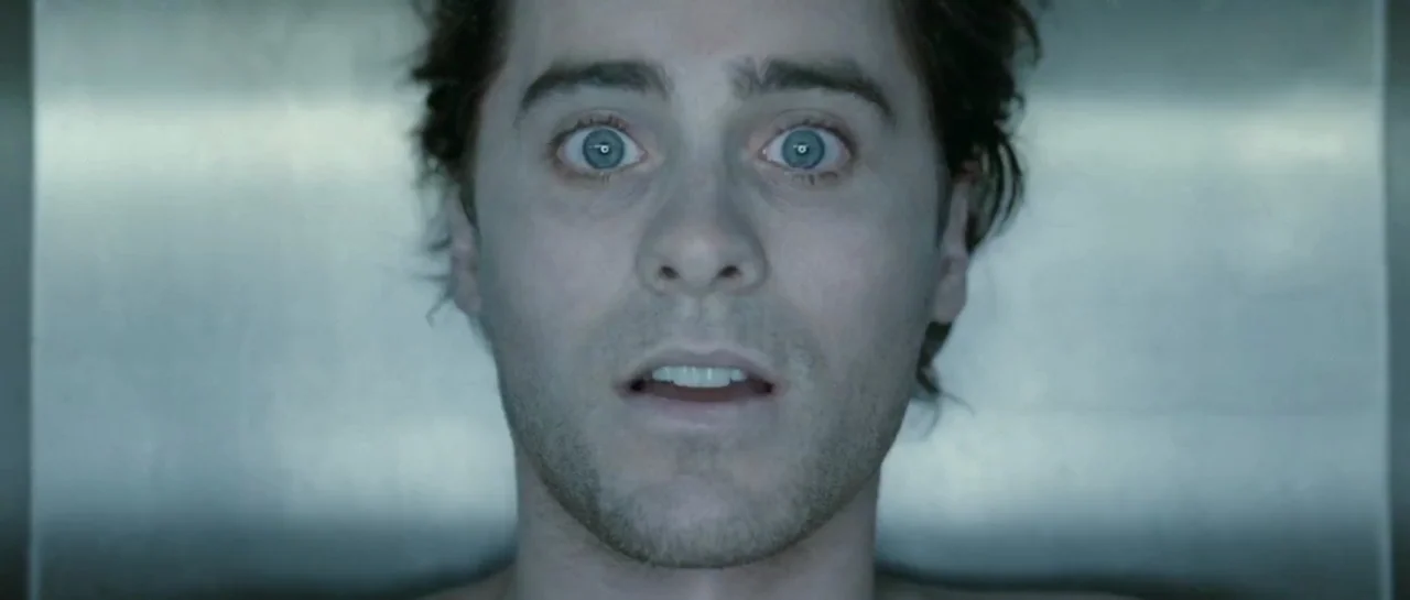 Mr. Nobody (2009) movie still: closeup — A man lies flat on a cold stainless steel slab in a sterile room. He stares upward with wide eyes.