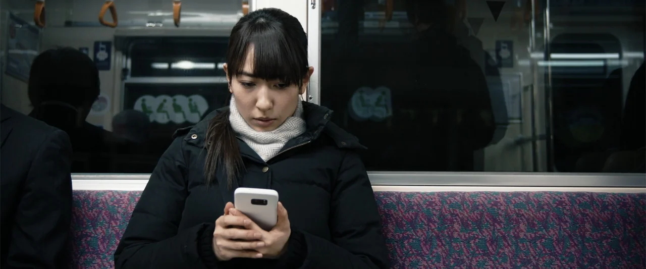 To Hear the Birds Singing (1995) movie still: medium — A passenger sits in a dark train carriage with purple patterned seats. A woman in a black…