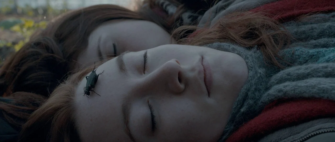 Byzantium (2012) movie still: closeup — Two women rest with their eyes closed in an outdoor field setting. A small black beetle crawls across the…