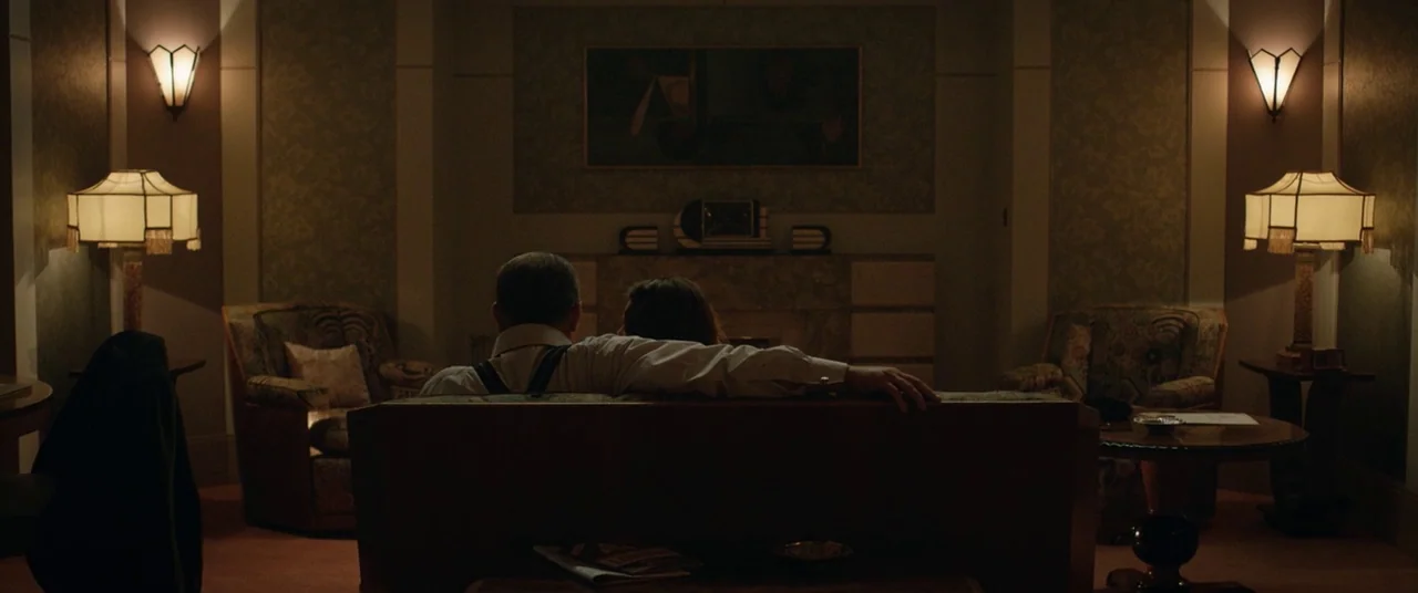 Domino (2005) movie still: medium — A 1940s living room features art deco wall sconces and matching symmetrical table lamps. A man and a woman sit…