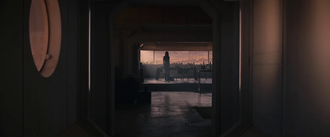 Settlers (2021) movie still: wide — A dark, futuristic habitation module with a large panoramic window overlooking a desert landscape. A woman…