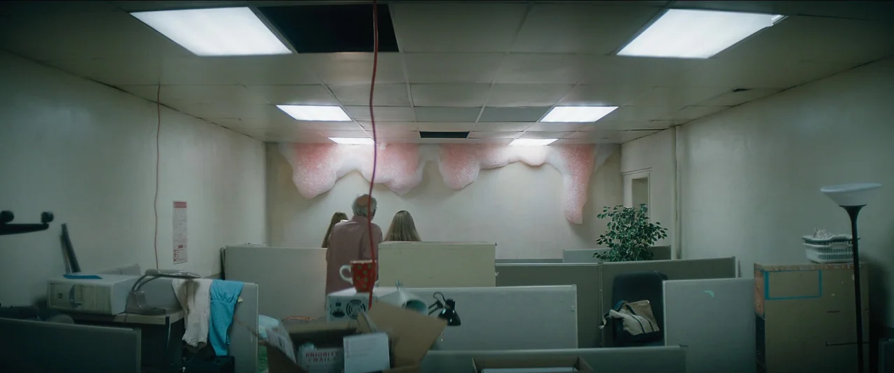 Kajillionaire (2020) movie still: wide — An office interior features beige cubicle partitions and drop ceiling panels with fluorescent lighting.…