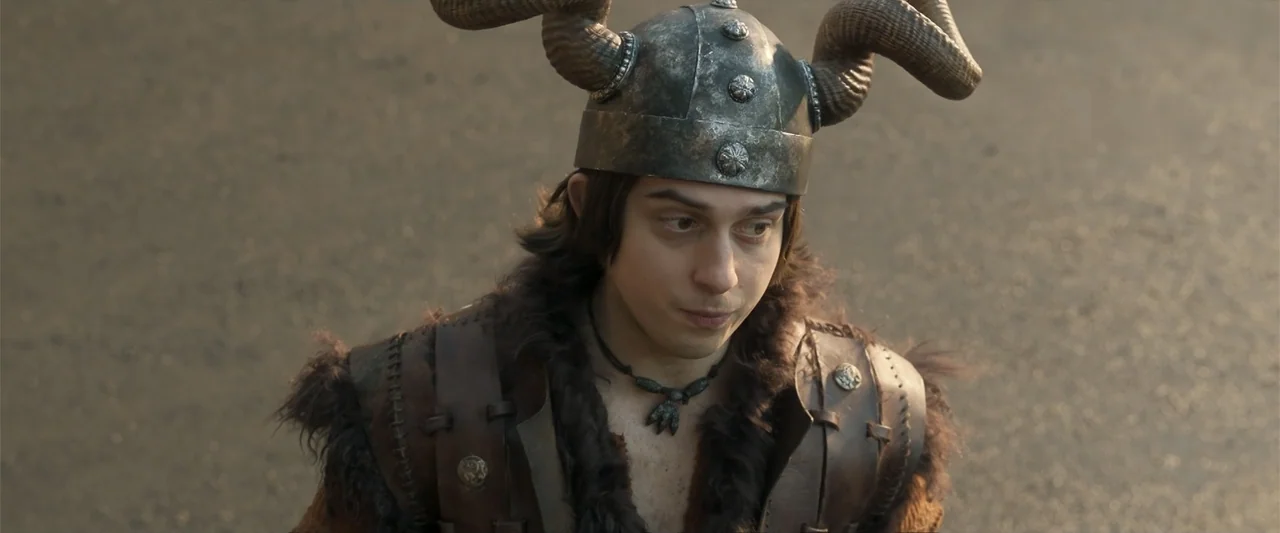 How to Train Your Dragon (2025) movie still: medium — A person wearing a horned metal helmet and fur-trimmed leather armor stands outdoors. The…