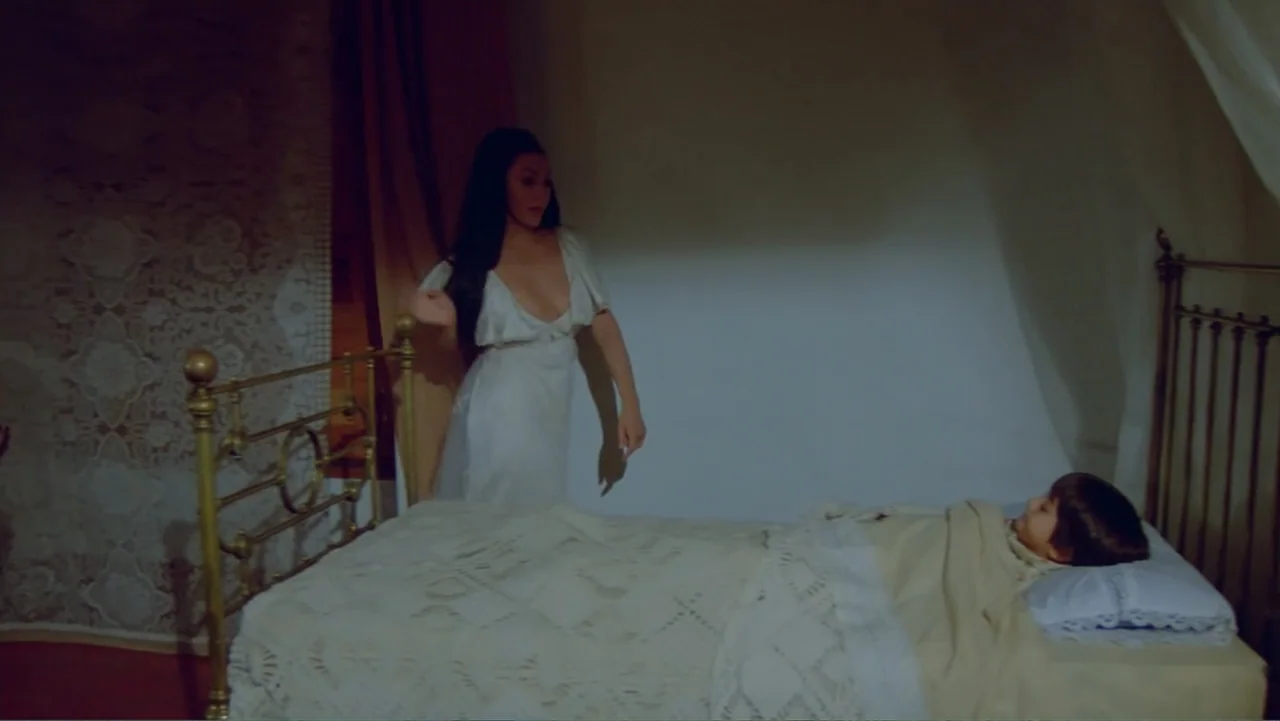 Toña Machetes (1985) movie still: medium — A quiet bedroom features an antique metal bed frame with white lace bedding. A woman in a light dress…