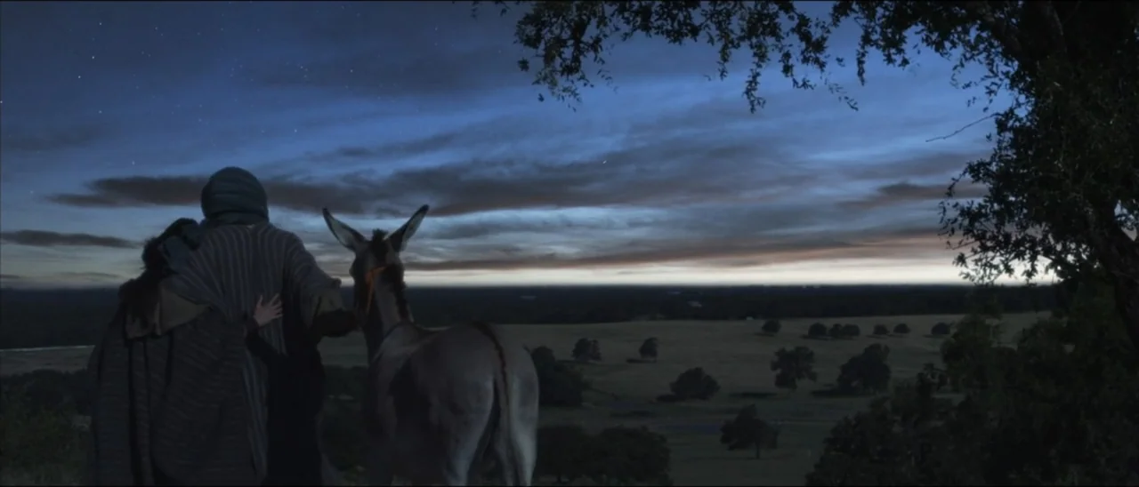 The Penitent Thief (2021) movie still: wide — An elevated hillside at dusk overlooks an expansive landscape of scattered trees and plains. Two robed…