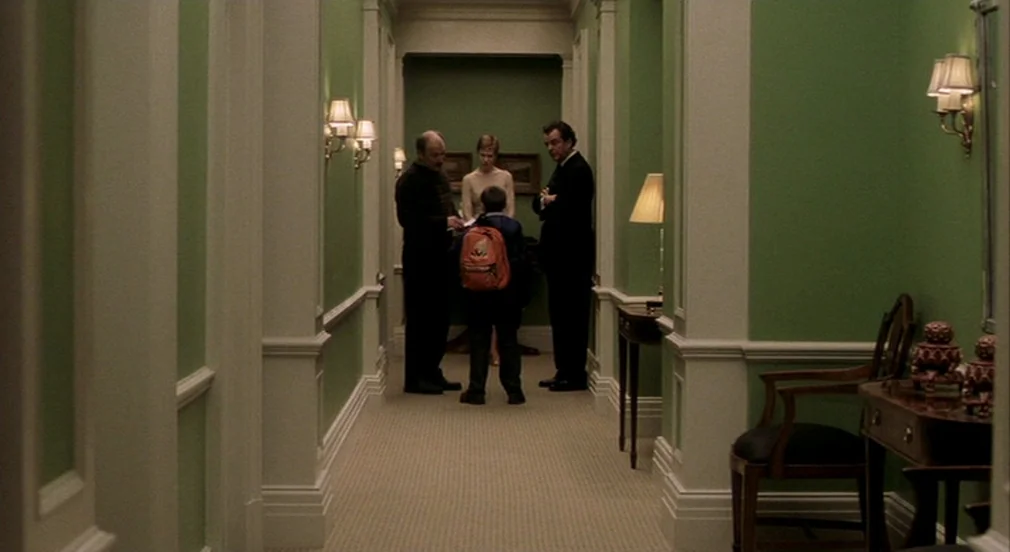 Birth (2004) movie still: fullbody — A long hallway with green walls and white wainscoting extends between two rooms. Four people gather in the…