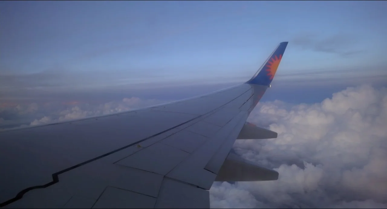 Federica Pellegrini - Underwater (2022) movie still: wide — An airplane wing extends into the frame over a thick layer of clouds. The sky shows the…