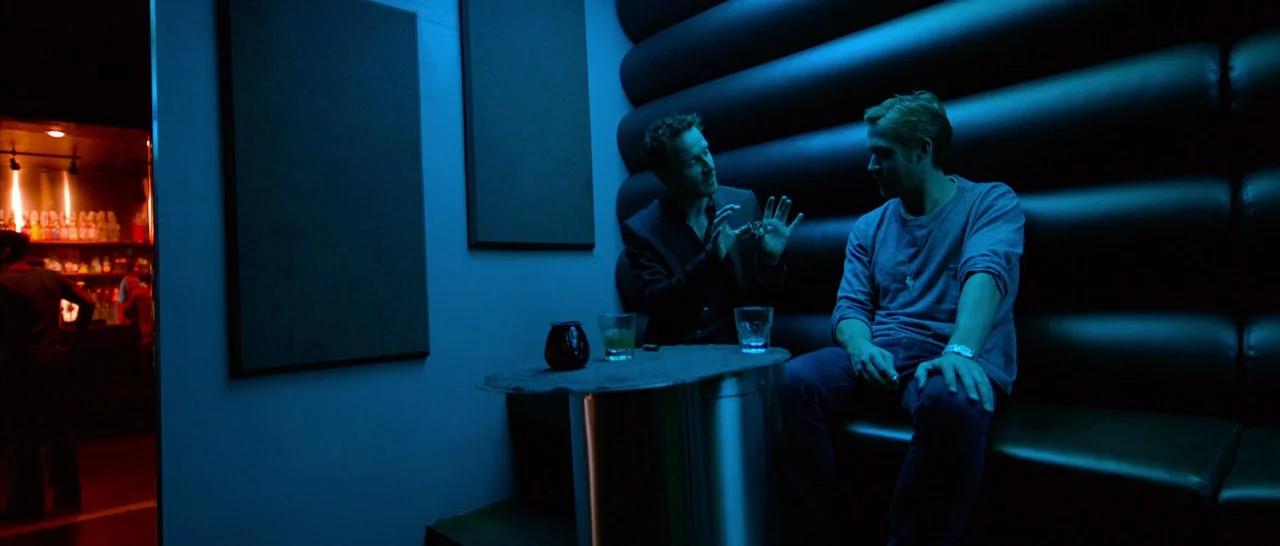 Song to Song (2017) movie still: medium — A dark lounge booth with leather padded walls is bathed in deep blue light. Two men sit across from each…