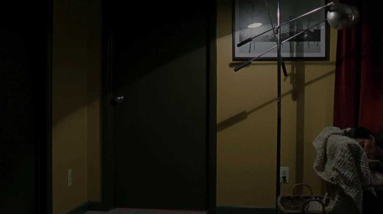 Lady in the Water (2006) movie still: medium — A dimly lit wall features a framed landscape print hung above a standing lamp. A woman sits in the…